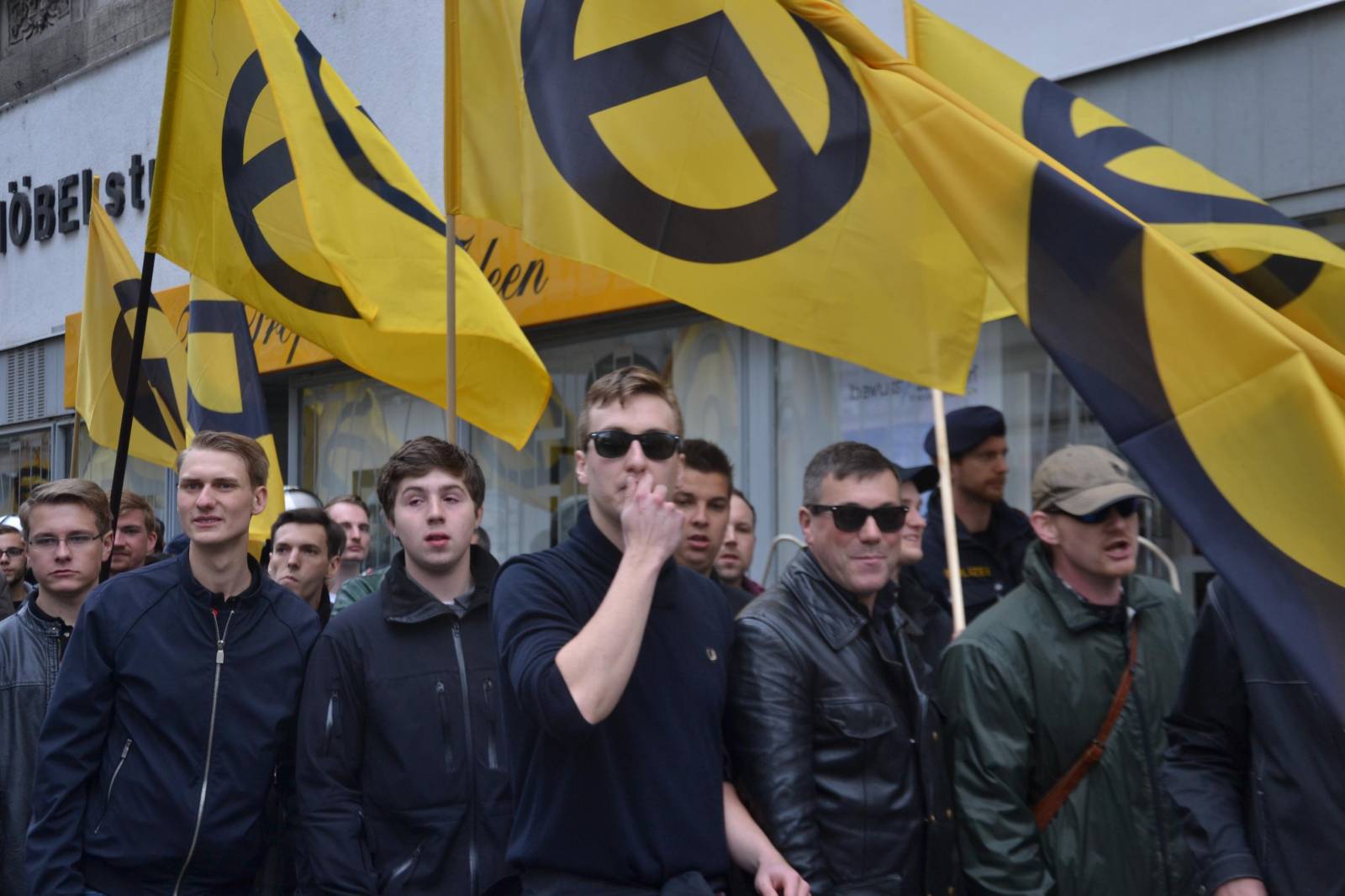 Bild zeigt Demonstration der IB in Wien 2014. Viele Männer zu sehen in schwarzer Kleidung, mehrer gelbe Flaggen sind abgebildet mit dem schwarzen IB-Logo.